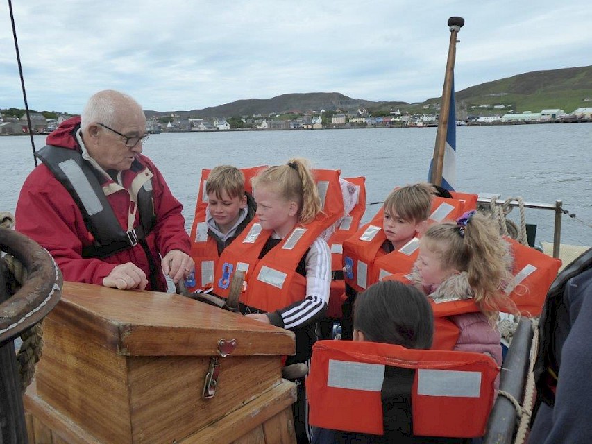 Trustee Brian Wishart explaining how the ships wheel controls the rudder to children from the Scalloway Peerie Club